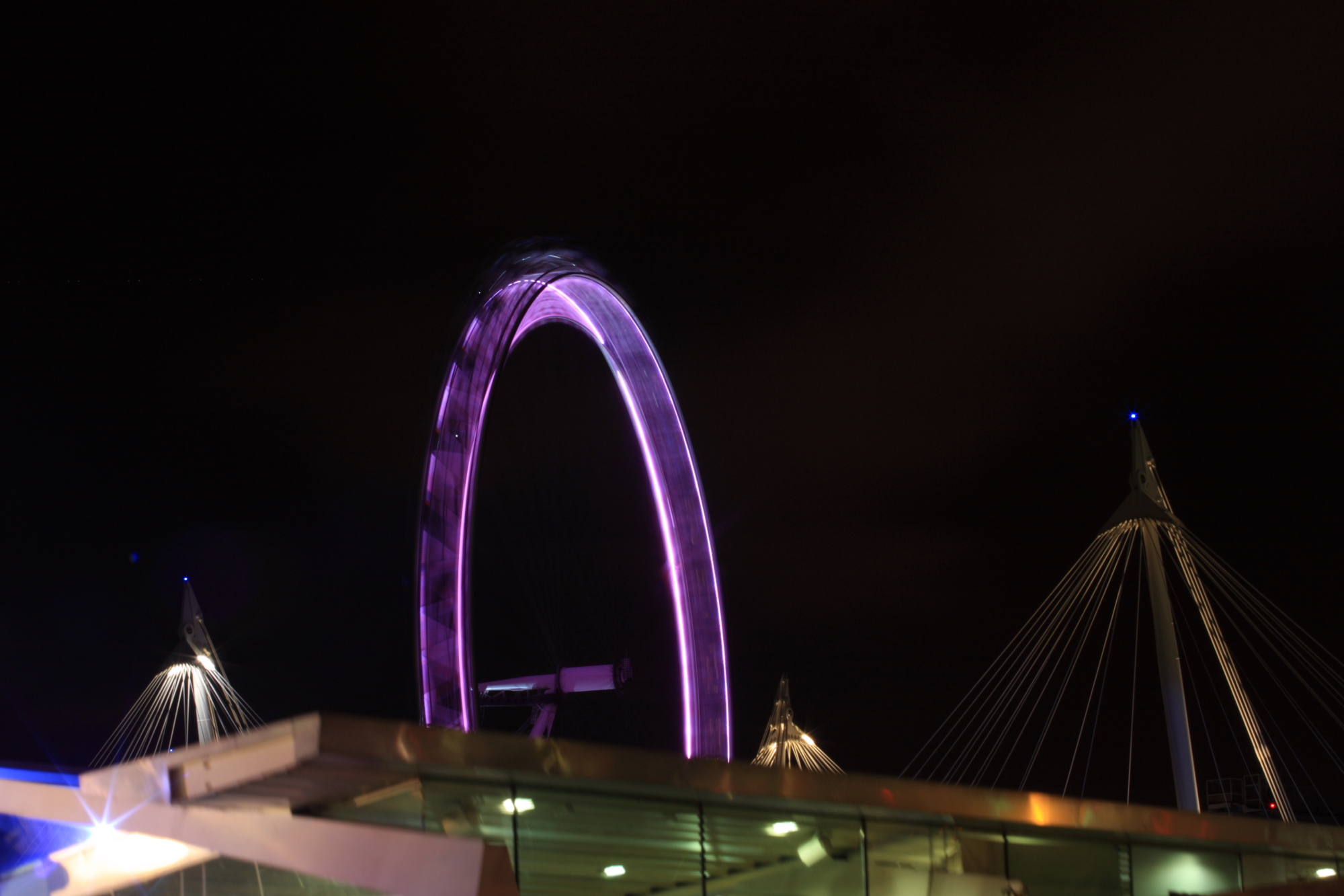 A purple London Eye spinning at night.